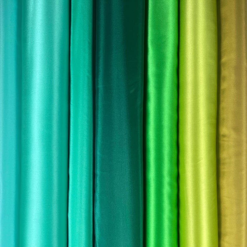 May include: A vertical display of various shades of green fabric. The colors range from a light teal to a deep forest green, with a few shades of lime and olive green. The fabric appears to be a smooth, satin-like material.
