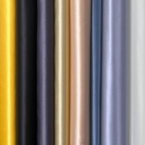 May include: A close-up of a collection of rolled fabric in various colors. The colors include yellow, black, navy, gold, peach, blue, lavender, and white. The fabric has a smooth, shiny texture.