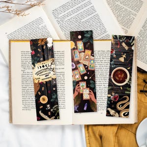 Könnte beinhalten: Vier Lesezeichen mit dunklem Hintergrund und bunten Illustrationen. Die Lesezeichen zeigen ein Ouija-Brett, Tarotkarten, eine Zaubertrankflasche und eine Schlange. Der Text auf dem Ouija-Brett lautet "ABCDEFGHIJKLMNOPQRSTUVXYZ 0123456789 YES GOODBYE".