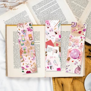 Könnte beinhalten: Drei farbenfrohe Lesezeichen mit rosa Hintergrund und verschiedenen Illustrationen. Die Lesezeichen zeigen Tarotkarten, eine Kristallkugel, eine Waage der Gerechtigkeit und andere dekorative Elemente.