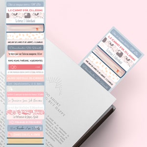 Könnte beinhalten: Bunte Lesezeichen mit französischen Buchtiteln wie "LE CARNET D'OR" und "UNE SOIF DE LIVRES ET DE LIBERTÉ". Die Lesezeichen stecken in einem Buch mit dem Text "LIFE IS TOO SHORT BUT HAPPY".