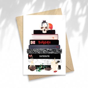 Könnte beinhalten: Grußkarte mit einem Stapel illustrierter Bücher, einem Totenkopf und anderen gotischen Elementen. Die Bücher tragen die Titel "Thriller" und "Horror". Eine Kerze, eine Zaubertrankflasche und Federn befinden sich am unteren Rand. Die Karte befindet sich auf weißem Hintergrund mit einem braunen Umschlag.