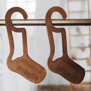 May include: Two wooden sock-shaped hangers with hooks. The hangers have a pattern of holes and numbers on the front.