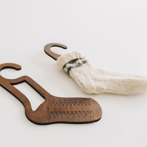 May include: Two wooden sock knitting tools with a hook at the top and a numbered scale on the bottom. One tool has a white and black striped sock hanging on it.