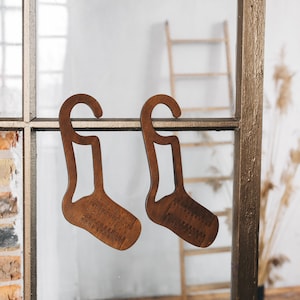 May include: Two wooden sock holders shaped like socks hanging on a window frame. The holders are brown and have a hook at the top.