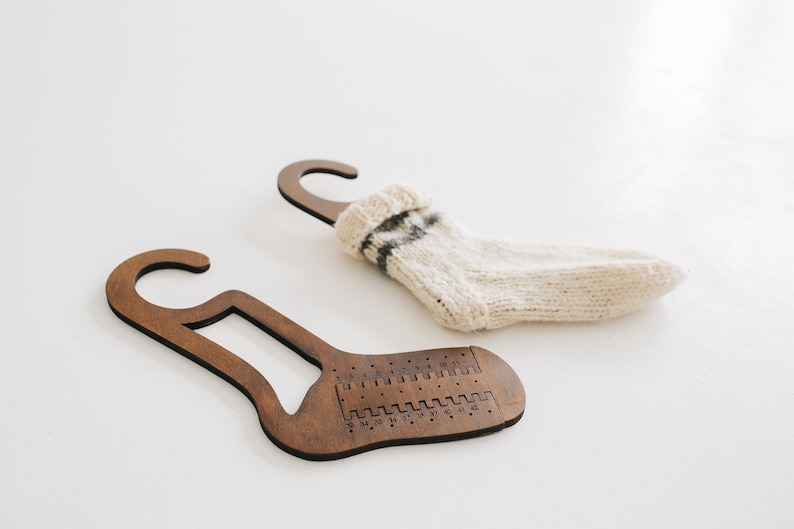 May include: Two wooden sock hangers with a hook at the top. One hanger has a white sock with black stripes hanging on it. The other hanger has a numbered scale on the bottom.