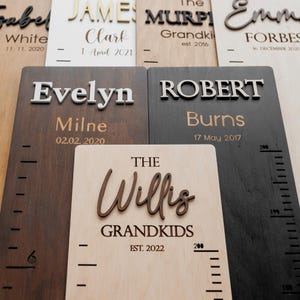 May include: Wooden growth charts with names and dates. The charts are in various shades of brown and black, with white or gold lettering. Some charts include the text "The Willis Grandkids EST. 2022". Each chart has a height measurement scale.
