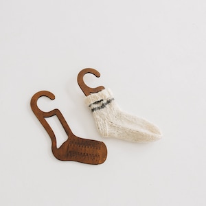 May include: Two wooden sock hangers with a white knitted sock hanging on one of the hangers.