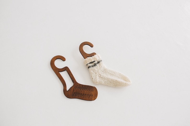 May include: Two wooden sock hangers with a white knitted sock hanging on one of the hangers.
