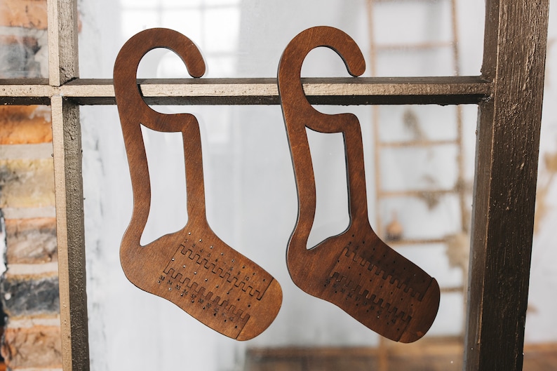 May include: Two wooden sock-shaped hangers with hooks. The hangers have a pattern of holes and numbers on the front.