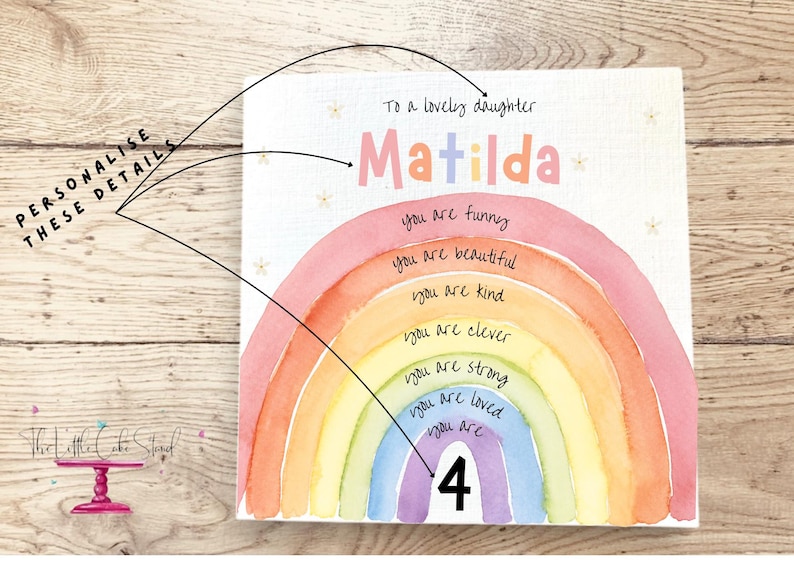 May include: A square white sign featuring a watercolor rainbow with the text To a lovely daughter, Matilda, and the phrases you are funny, you are beautiful, you are kind, you are clever, you are strong, you are loved, you are 4.