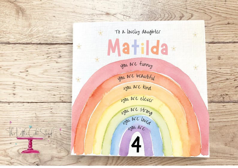 May include: A square greeting card featuring a watercolor rainbow with the text To a lovely daughter Matilda at the top. The rainbow stripes contain the phrases you are funny, you are beautiful, you are kind, you are clever, you are strong, you are loved, and you are 4.