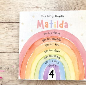 May include: A square greeting card featuring a watercolor rainbow with the text To a lovely daughter Matilda at the top. The rainbow stripes contain the phrases you are funny, you are beautiful, you are kind, you are clever, you are strong, you are loved, and you are 4.