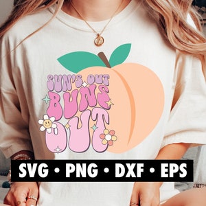 May include: A white t-shirt with a peach graphic and the text "Sun's Out Buns Out" in a retro font. The peach is pink and has a green leaf.