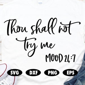 May include: White t-shirt with black text that reads "Thou shall not try me MOOD 24:7". The shirt is displayed on a white wooden background with a pair of white sneakers and blue jeans.