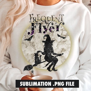 以下が含まれることがあります： 満月を背景に、ほうきに乗って飛ぶ魔女のグラフィックデザインが施された白いスウェットシャツ。魔女の上に「Frequent Flyer」という文字が書かれています。デザインはヴィンテージ調で、使い古したような風合いになっています。