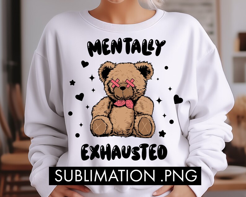 May include: White sweatshirt with a brown teddy bear wearing pink eye patches and a pink bow tie. The text "Mentally Exhausted" is printed in black on the sweatshirt.