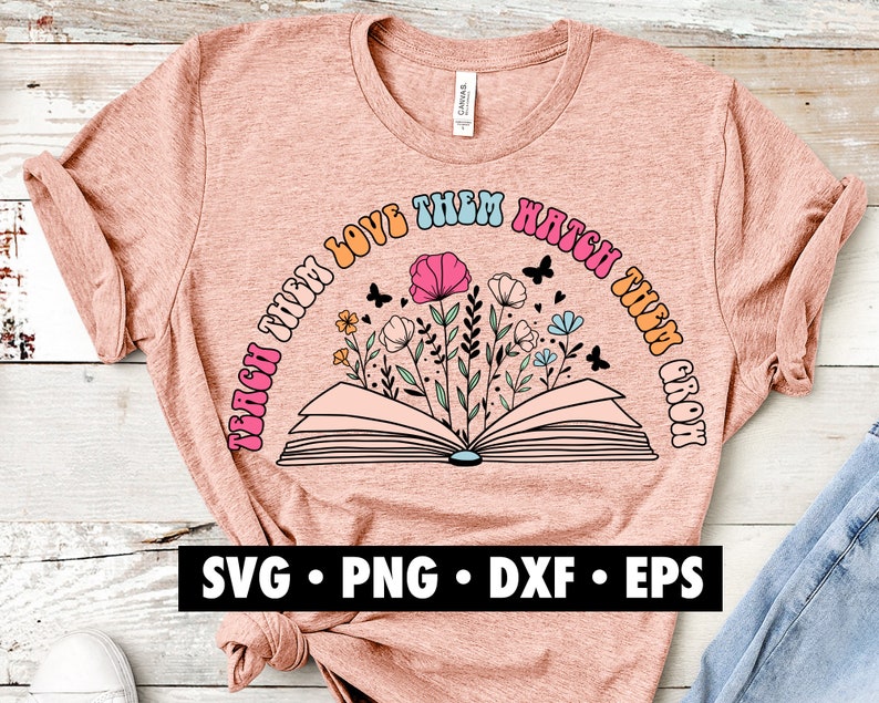 K&ouml;nnte beinhalten: Ein pinkfarbenes T-Shirt mit einem Grafikdesign eines offenen Buches mit Blumen und dem Text "Teach them love them watch them grow".