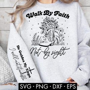 May include: A light gray sweatshirt with the text "Walk By Faith Not By Sight" in black script. The design includes a cowboy boot filled with flowers. The sleeve features the text "He Guides My Steps I will not stumble" and a cross.