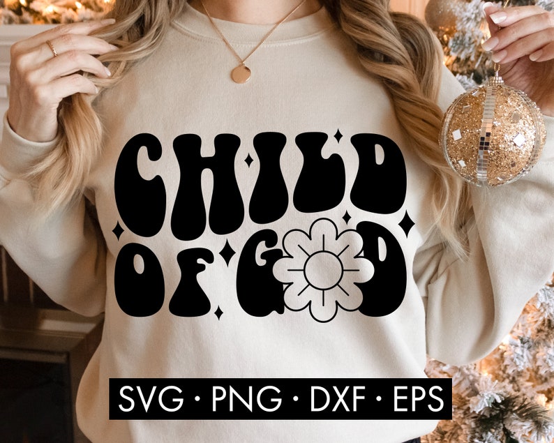 May include: A beige sweatshirt with the text "CHILD OF GOD" in black, retro-style lettering. A stylized flower is centered below the text. The sweatshirt is being worn by a person.