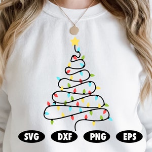 Może przedstawiać: Biała bluza z nadrukiem choinki. Drzewko to czarny kontur z kolorowymi światełkami i żółtą gwiazdą. Na dole bluzy znajdują się słowa "SVG", "DXF", "PNG" i "EPS" w czarnych owalach.