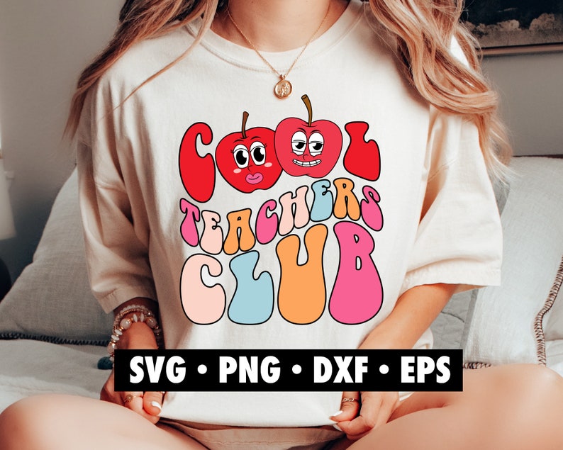 K&ouml;nnte beinhalten: Ein wei&szlig;es T-Shirt mit einem bunten Grafikdesign, auf dem "Cool Teachers Club" steht. Die Grafik zeigt zwei Comic-&Auml;pfel mit Gesichtern und einer Retro-Schriftart.