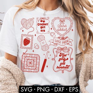 May include: White t-shirt featuring red crochet-themed graphics, including yarn balls, a crochet hook, and text that reads "Crochet girl era," "Yarn addict," and "Hot girls get hooked." The shirt also has a strawberry stamp design.