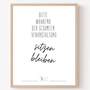Pode incluir: Uma impressão emoldurada com uma moldura de madeira clara. O fundo branco apresenta texto preto que diz "Bitte während der gesamten Veranstaltung sitzen bleiben."