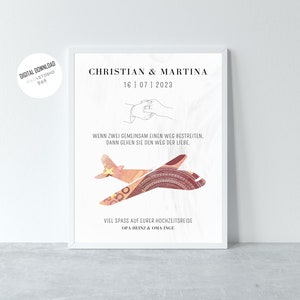 K&ouml;nnte beinhalten: Ein wei&szlig;er gerahmter Druck mit einer Schwarzwei&szlig;illustration von zwei sich haltenden H&auml;nden. Der Text "Christian & Martina" befindet sich oben auf dem Druck, darunter das Datum "16 | 07 | 2023". Der Text "Wenn zwei gemeinsam einen Weg bestreiten. Dann gehen sie den Weg der Liebe." befindet sich unter der Illustration. Der Druck zeigt auch eine rote und wei&szlig;e Flugzeugillustration mit dem Text "Viel Spass auf eurer Hochzeitsreise Opa Heinz & Oma Inge" unten.