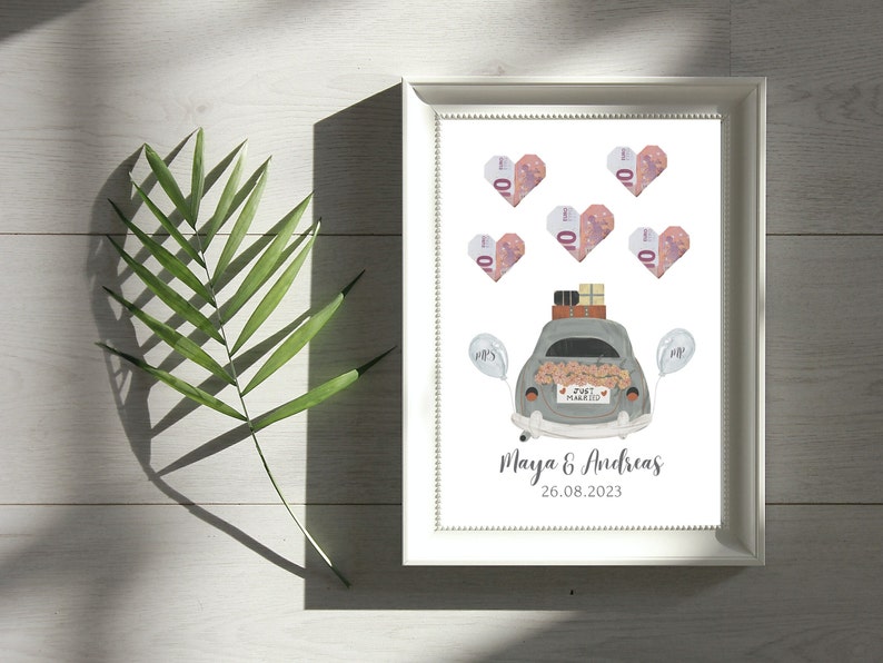 May include: A white picture frame with a white background. The frame contains a drawing of a gray car with a "Just Married" sign on the back. The car is decorated with flowers and has luggage on the roof. There are pink hearts with the number 10 on them around the car. The text "Maya & Andreas 26.08.2023" is at the bottom of the frame.