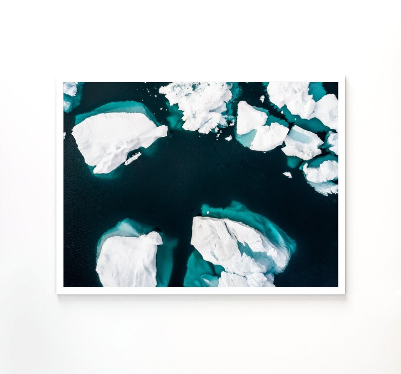 May include: Aerial view of a turquoise blue body of water with white icebergs floating on the surface.
