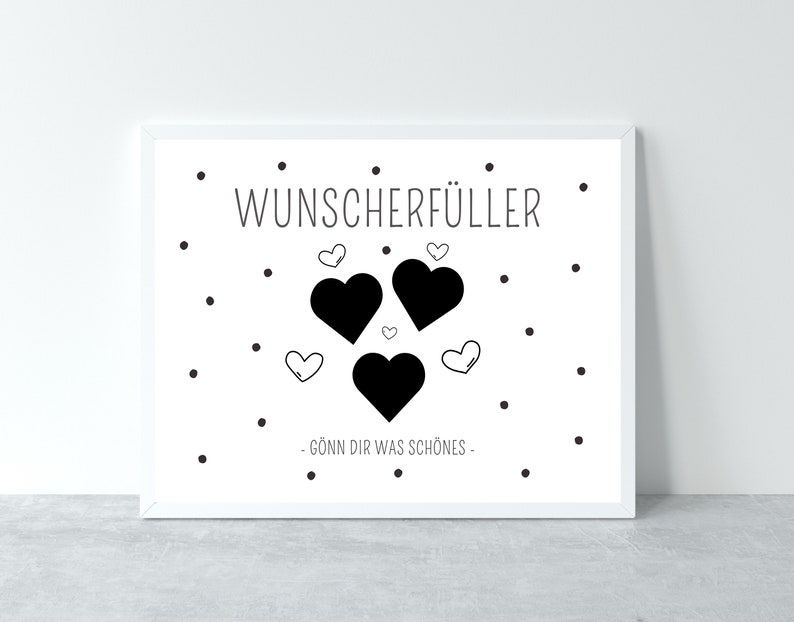 May include: A white framed print with black text that reads "Wunsch erf&uuml;ller" and a graphic of three black hearts with smaller white hearts inside. The text below the hearts reads "G&ouml;nn dir was sch&ouml;nes."