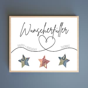 May include: A white card with black text that reads "Wunschersch&ouml;pfer" with a heart drawn around the text. The text "HAPPY BIRTHDAY" is written on the left side of the heart and "THOMAS" is written on the right side of the heart. Three stars are placed below the heart, each made of a 50 Euro bill.