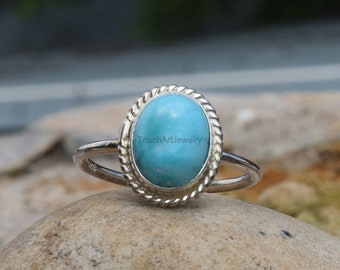 May include: A silver ring with a blue turquoise stone set in a rope-like border.