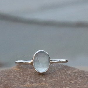 Peut inclure: Une bague en argent avec une pierre précieuse ovale, bleu clair et facettée. La bague est montée sur un anneau simple et repose sur une surface brune texturée. La pierre précieuse est le point central, captant la lumière et ajoutant une touche d'élégance.