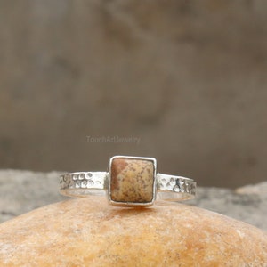 May include: A silver ring with a square, brown and white stone set in the center. The band of the ring is textured.