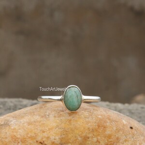 May include: A silver ring with a light green oval gemstone. The ring is on a light brown rock.