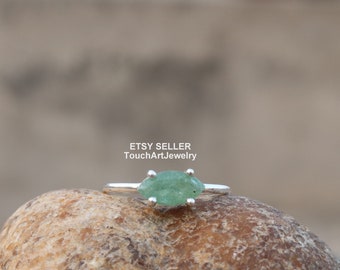 May include: A silver ring with a green gemstone set in a marquise shape. The ring is on a brown rock.
