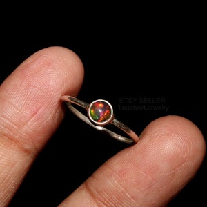 Könnte beinhalten: Ein silberner Ring mit einem runden, rot-orange-schwarzen Opal-Edelstein. Der Ring befindet sich an einem Finger.