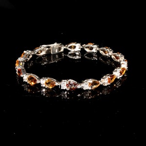 May include: A silver bracelet with a row of pear-shaped orange gemstones and smaller clear gemstones.
