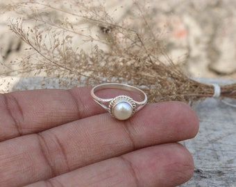 May include: A silver ring with a white pearl set in a twisted band.