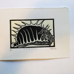 Op de afbeelding: Zwart-witte houtsnede van een gestileerd wezen met een stekelige kroon. De print is getiteld "Naked Lunch" en genummerd 1/20.