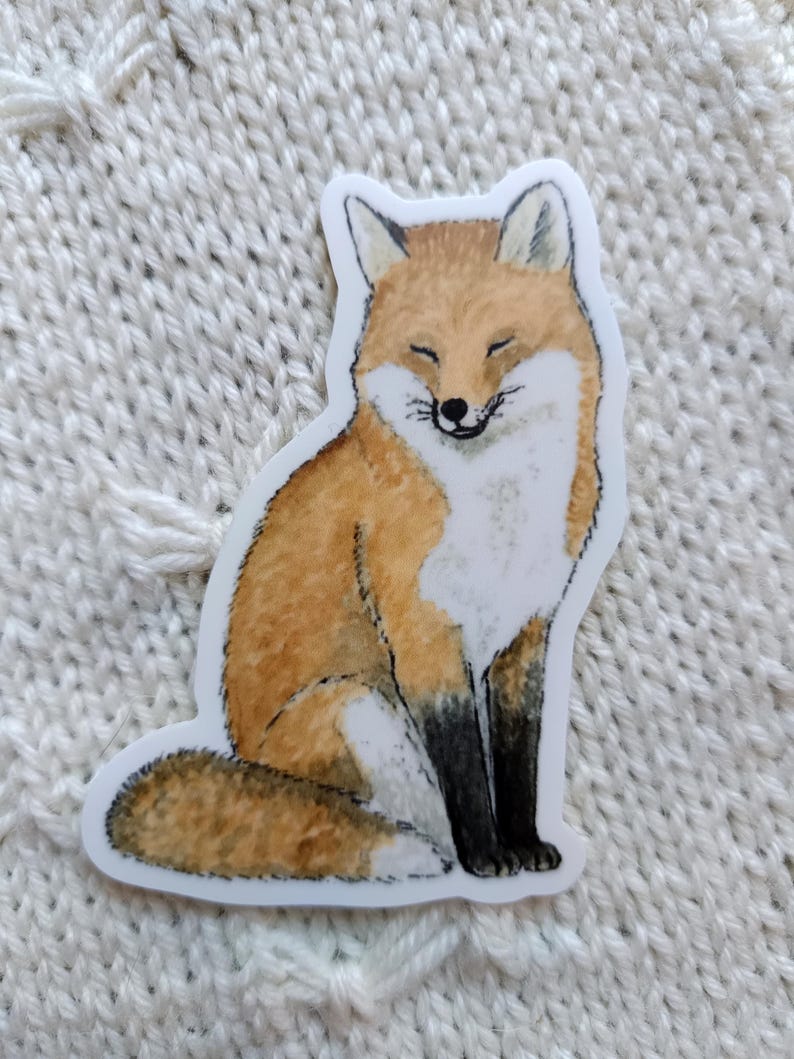 Op de afbeelding: Een sticker met een glimlachende vos met oranje en witte vacht en zwarte poten. De vos zit met gesloten ogen. De sticker heeft een witte rand.