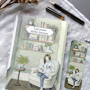 Può includere: Un diario e un segnalibro con l'illustrazione di una persona che legge in poltrona. Il diario presenta la scritta "Taccuino delle letture". È visibile anche una penna nera con dettagli dorati.