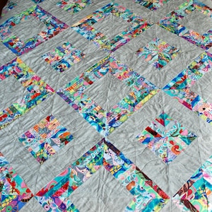 May include: A gray quilt with a diamond pattern. The diamonds are made of colorful fabric scraps sewn together. The quilt is quilted with a simple straight stitch.