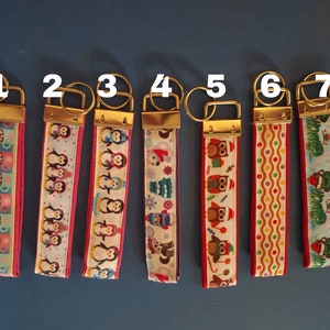 May include: A collection of seven keychains with various festive designs. Each keychain features a patterned ribbon with gold-colored hardware and a key ring. Designs include penguins, owls, and holiday-themed patterns.