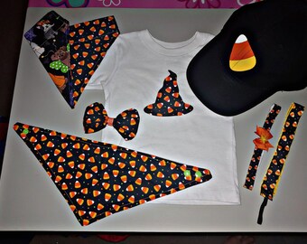 Puede incluir: Un conjunto de disfraz de Halloween para un bebé o un niño pequeño, que incluye una camiseta blanca con una aplicación de sombrero de bruja, una gorra de béisbol negra con una aplicación de maíz dulce, una corbata de moño negra y naranja, dos bandanas negras y naranjas y dos diademas negras y naranjas con diseños de maíz dulce.