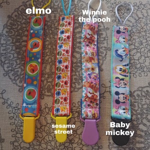 Puede incluir: Cuatro mordedores de bebé de tela coloridos con diferentes diseños de personajes. Los mordedores están etiquetados como "Elmo", "Sesame Street", "Winnie the Pooh" y "Baby Mickey".