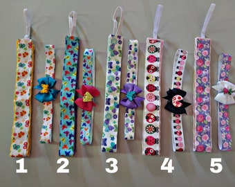 May include: Five fabric headbands with decorative bows. The headbands display patterns of butterflies, ladybirds, and floral designs. Each headband has a white elastic loop. The headbands are numbered 1 to 5.