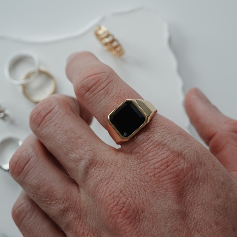 Ein Mann trägt den vergoldeten Siegelring mit schwarzem Onyx an der Hand. Das Accessoire unterstreicht seinen maskulinen und eleganten Stil.